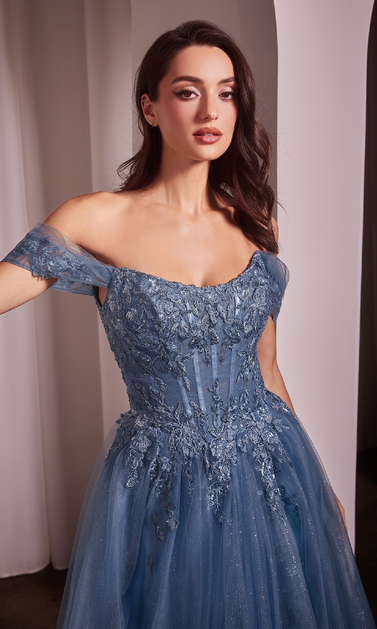Woman modeling the Ladivine CD799 off-shoulder long prom dress in blue lace and tulle with floral embroidery, standing indoors against a neutral backdrop.